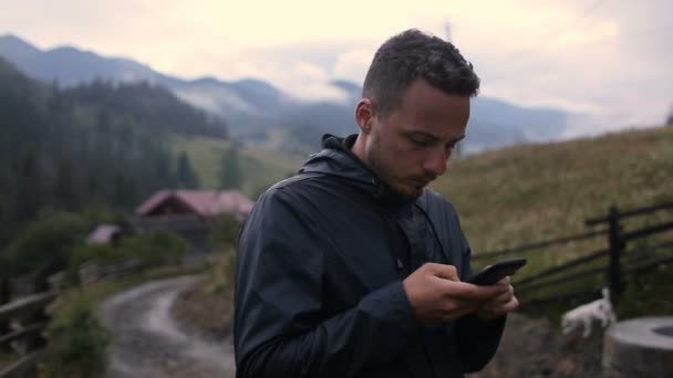 Egy fiatal férfi ír egy SMS-t az esti órákban, a hegyekben. A következő reptér környékén: az erdő, a ködben — Stock videók