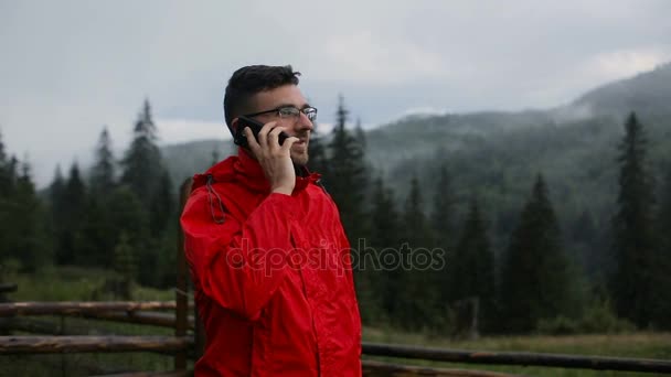 Egy fiatalember beszél a telefonon esténként a hegyekben. A következő reptér környékén: az erdő, a ködben — Stock videók