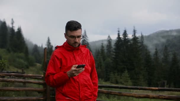 En ung man skriver ett Sms på kvällen i bergen. Runt i skogen i dimman — Stockvideo