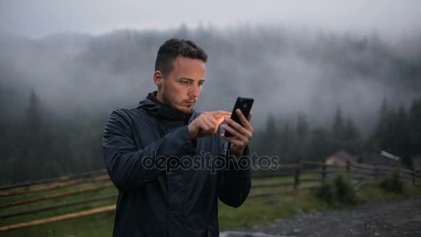 Mladý muž použít telefon večer v horách. Po lese v mlze — Stock video