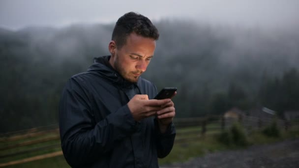 Un jeune homme écrit un SMS le soir dans les montagnes. Autour de la forêt dans le brouillard 