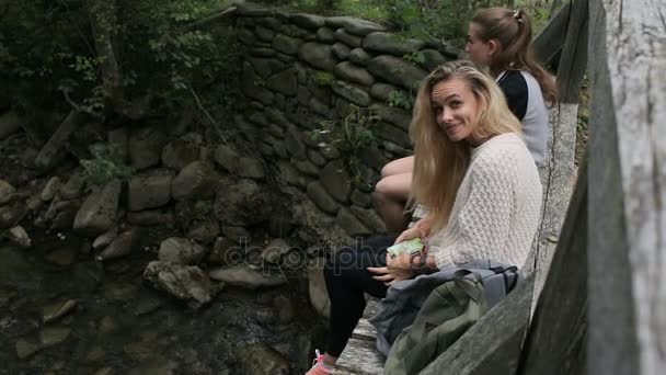 Junge Mädchen sitzen auf einer Brücke über einen Gebirgsfluss — Stockvideo