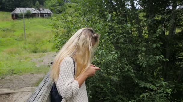 Jeune fille avec un téléphone sur un pont au-dessus d'une rivière de montagne — Video