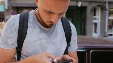 Sakallı dışında korkuluk ve posta üstünde hareket eden telefon kontrol üzerinde oturan genç adam