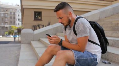 Genç adam şehir adımda oturur ve telefonda bir oyun oynuyor