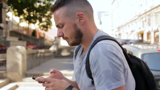 Młodego człowieka z brodą, siedząc na kroki poza i sprawdzanie poczty na telefonie komórkowym — Wideo stockowe