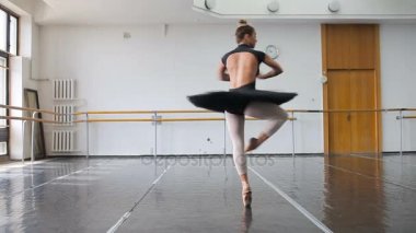 Siyah sırt çantalı profesyonel bir balerin büyük bir eğitim salonunda dans ediyor.