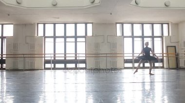 Siyah sırt çantalı profesyonel bir balerin büyük bir eğitim salonunda dans ediyor.