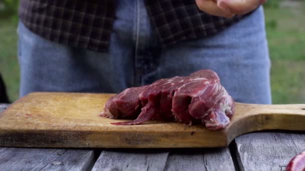 Um homem dá um pedaço de carne a um cão enquanto corta um bife — Vídeo de Stock