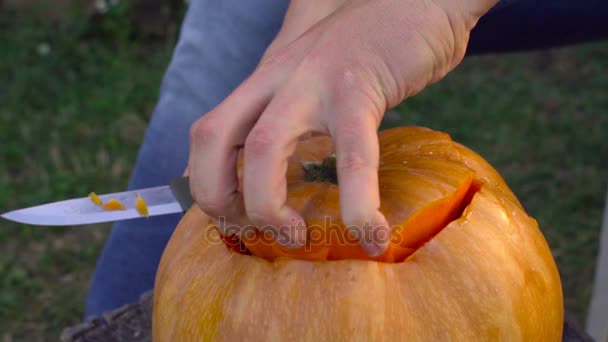 Man skär från en pumpa Jack-o-lantern i trädgården på en stubbe — Stockvideo