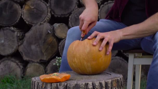 Hombre talla de una calabaza Jack-o-linterna en el patio trasero en un tocón de árbol — Vídeo de stock