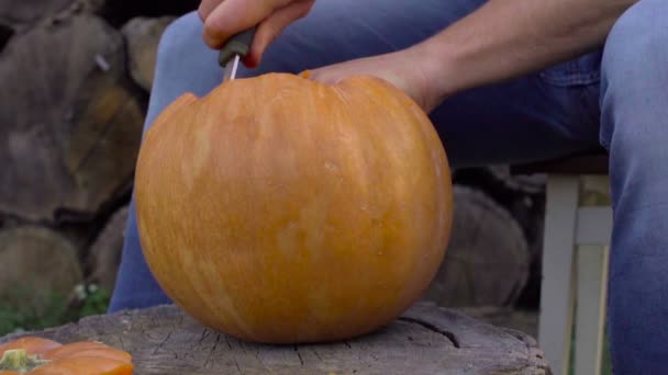 Hombre talla de una calabaza Jack-o-linterna en el patio trasero en un tocón de árbol — Vídeo de stock