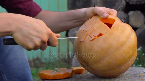 Hombre talla de una calabaza Jack-o-linterna en el patio trasero en un tocón de árbol — Vídeo de stock