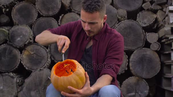 Hombre talla de una calabaza Jack-o-linterna en el patio trasero en un tocón de árbol — Vídeos de Stock