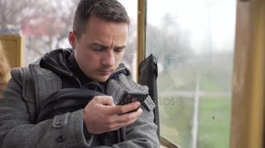 Genç bir adam bir tramvaya siting ve telefonunu kullanarak