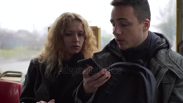 Young man and woman sitting in tram chatting about gadgets and sharing something online — Stock Video