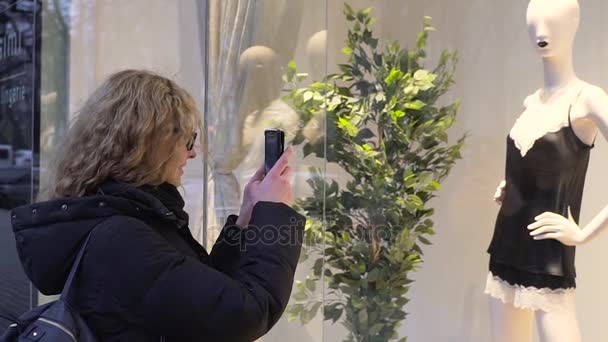 Mujer hermosa joven está fotografiando ropa interior en un escaparate en un teléfono inteligente — Vídeo de stock