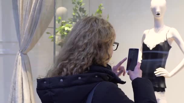 Jovem mulher bonita está fotografando roupas íntimas em uma vitrine em um smartphone — Vídeo de Stock