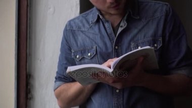 Pan bir karanlık oda ayakta pencerenin yanında kitap okuma adam