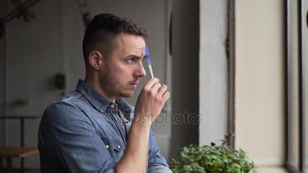 窓の近くのメモ帳に書く若いハンサムなゲイの男性のミディアム ショット — ストック動画