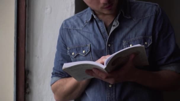 Pan de hombre leyendo libro en cuarto oscuro de pie junto a la ventana — Vídeos de Stock