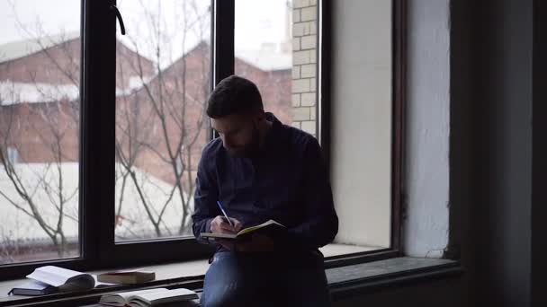 Pan van jonge man studeren zittend op de vensterbank — Stockvideo