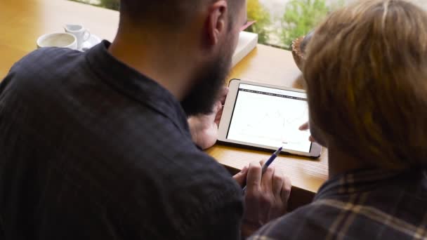 Primer plano del hombre y la mujer discuten el rendimiento financiero en una tableta mientras está sentado en un café — Vídeos de Stock