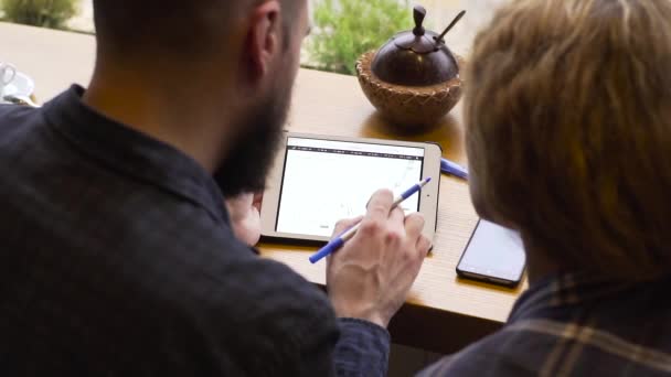 Gros plan d'un homme et d'une femme étudiant un graphique sur une tablette assis dans un café — Video