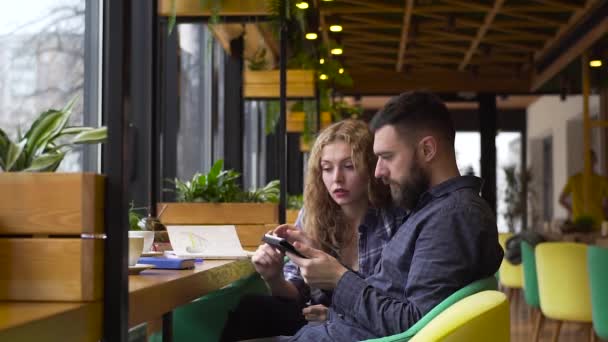 Zwolnionym tempie facet i dziewczyna omówienia ich uruchamiania z tabletem siedząc w kawiarni — Wideo stockowe