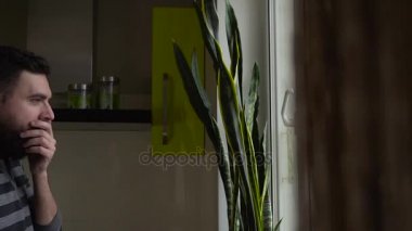 Orta genç adam kollarını esneme ve mutfak penceresinde yanında esnemek
