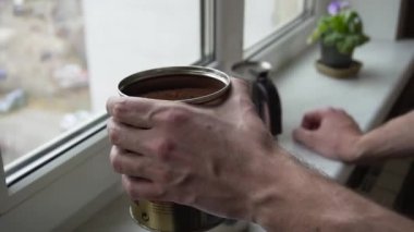 Sakallı genç adam çekilmiş kahve mutfakta bir pencere yakınında bir kavanoz ayakta koklama görüntüsünü kapatmak