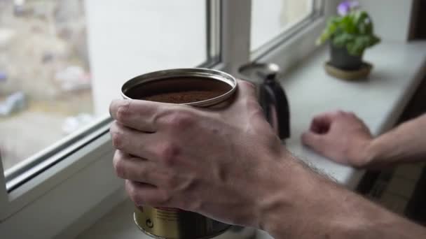 Close-up shot van bebaarde jongeman snuiven gemalen koffie in een pot staan in de buurt van een raam in de keuken — Stockvideo