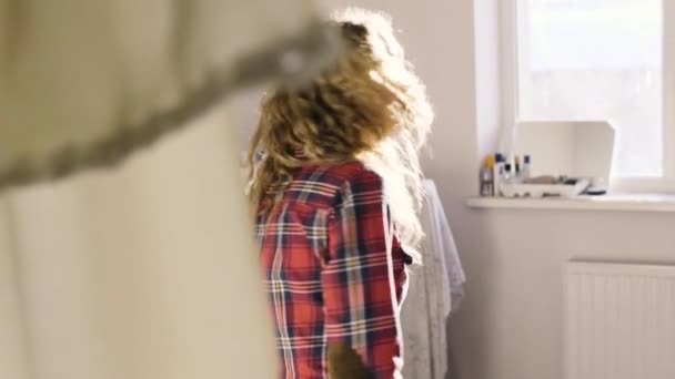 A girl walks through the curtain in a sunny room playing with her hair — Stock Video