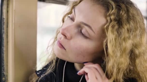Vacker kvinna lyssnar musik i hörlurar på smartphone Ridande spårvagnen — Stockvideo