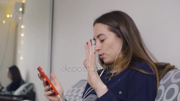 Een jonge vrouw is dansen op het bed luisteren naar muziek op de koptelefoon op een mobiele telefoon — Stockvideo