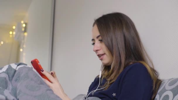 Mulher feliz bonita jovem sorrindo, falando em videochamada em um telefone celular no quarto durante o dia — Vídeo de Stock