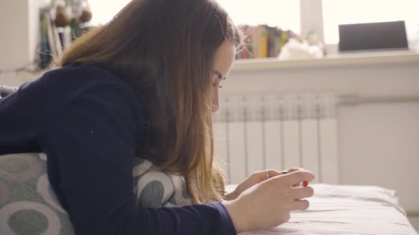 Unga kvinnor om på sängen spela smart telefon — Stockvideo