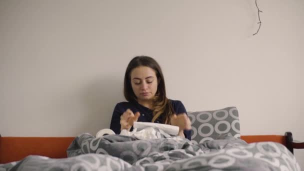 Mujer joven sonándose la nariz en papel tejido en la cama — Vídeo de stock