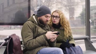 Genç erkek ve kadın bir otobüs durağında beklerken cep telefonu kullanmak