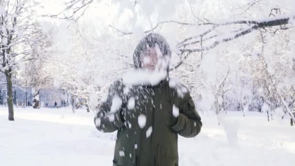 枝から雪が降っています。男は、フードで頭をカバーしています。スローモーション. — ストック動画