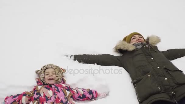 Liten flicka och hennes mamma gör en snöängel — Stockvideo
