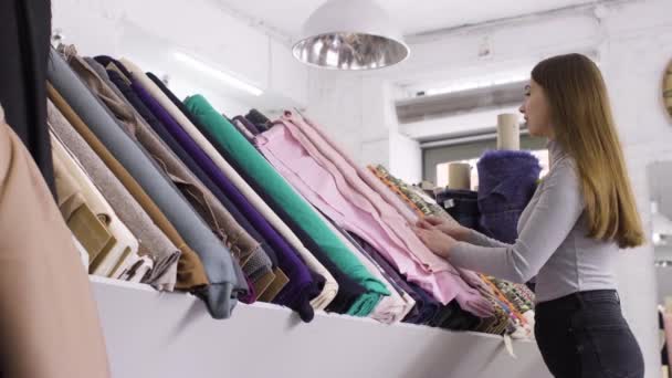 Young beautiful woman chooses the fabric in a textile shop — Stock Video