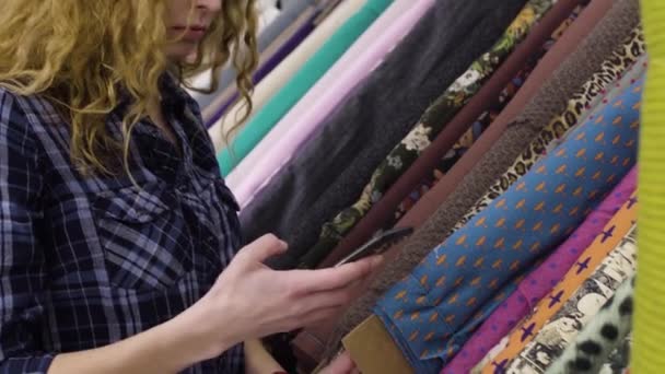 Mooie jonge vrouw kiest het weefsel in een textiel-winkel — Stockvideo