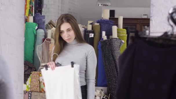 Una giovane ragazza sceglie un panno per un vestito vicino a uno specchio nell'atelier — Video Stock