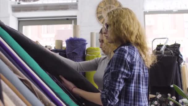 Zwei junge Frauen kaufen in einem Gewebegeschäft Stoffe. Lächeln, reden — Stockvideo
