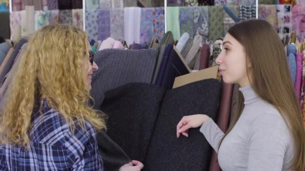 Twee jonge vrouwen kopen doek in een winkel van weefsel. Glimlachen, praten — Stockvideo