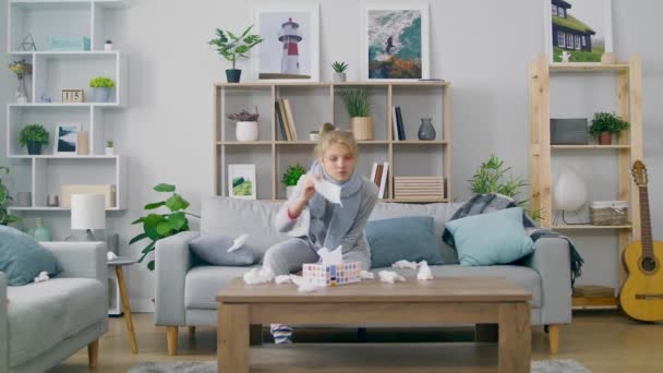 Girl with a cold sneezes while sitting on a couch in a living room — Stock Video