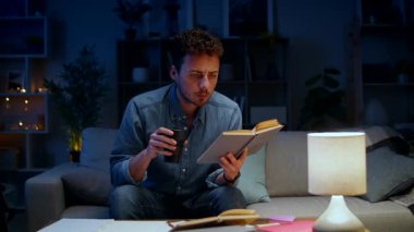 Genç adam akşamları evde çalışırken kitap okur ve kahve içer.