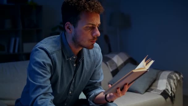 Young man reads a book and drinks coffee while studying in the evening — Stockvideo