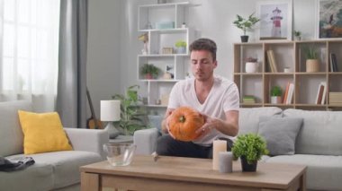 Genç bir adam balkabağını incelerken balkabağı kabağı oyuyor.